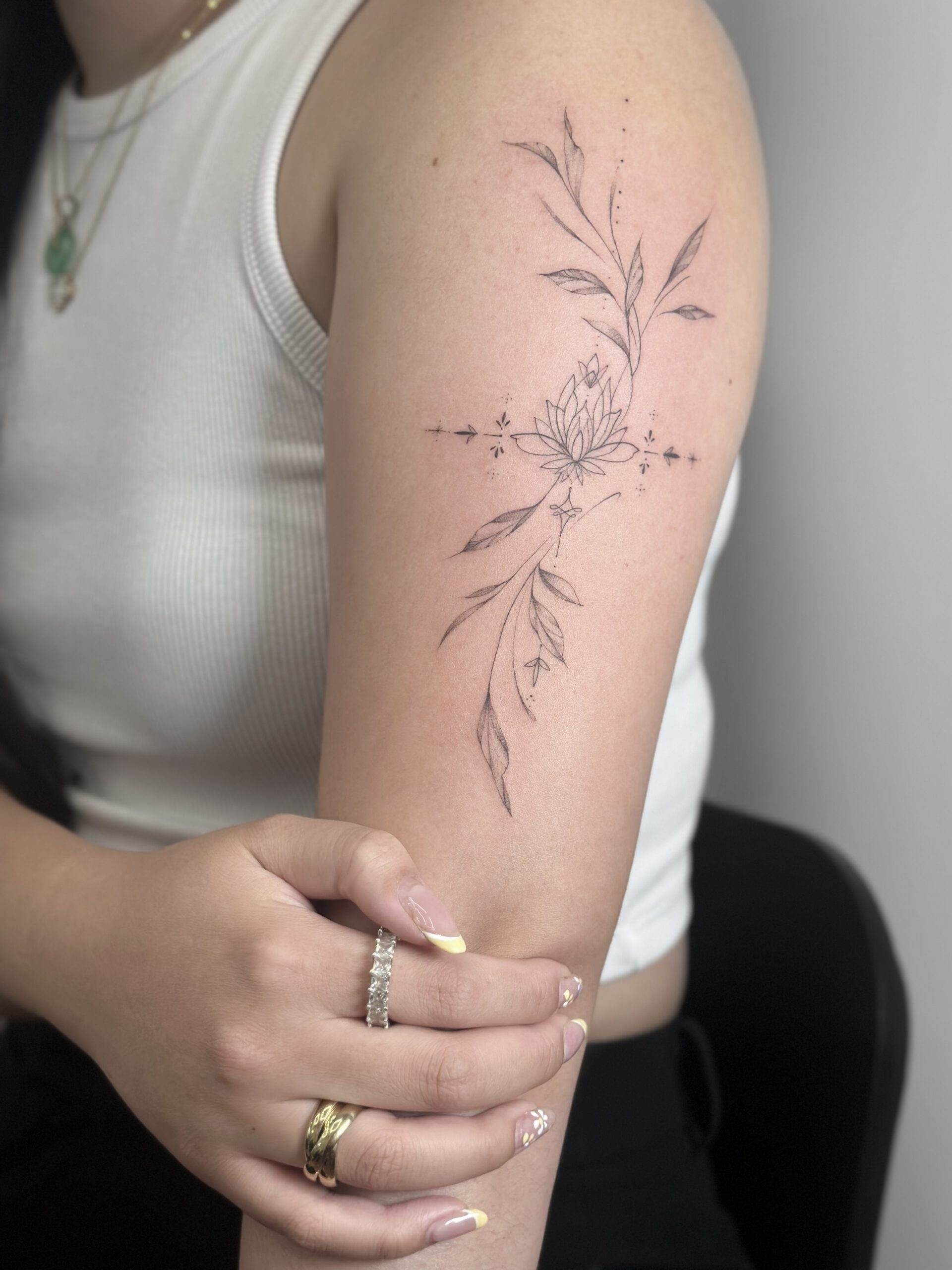 Botanisches fineline Tattoo mit Blüten und Blättern am Oberarm in Berlin-Charlottenburg