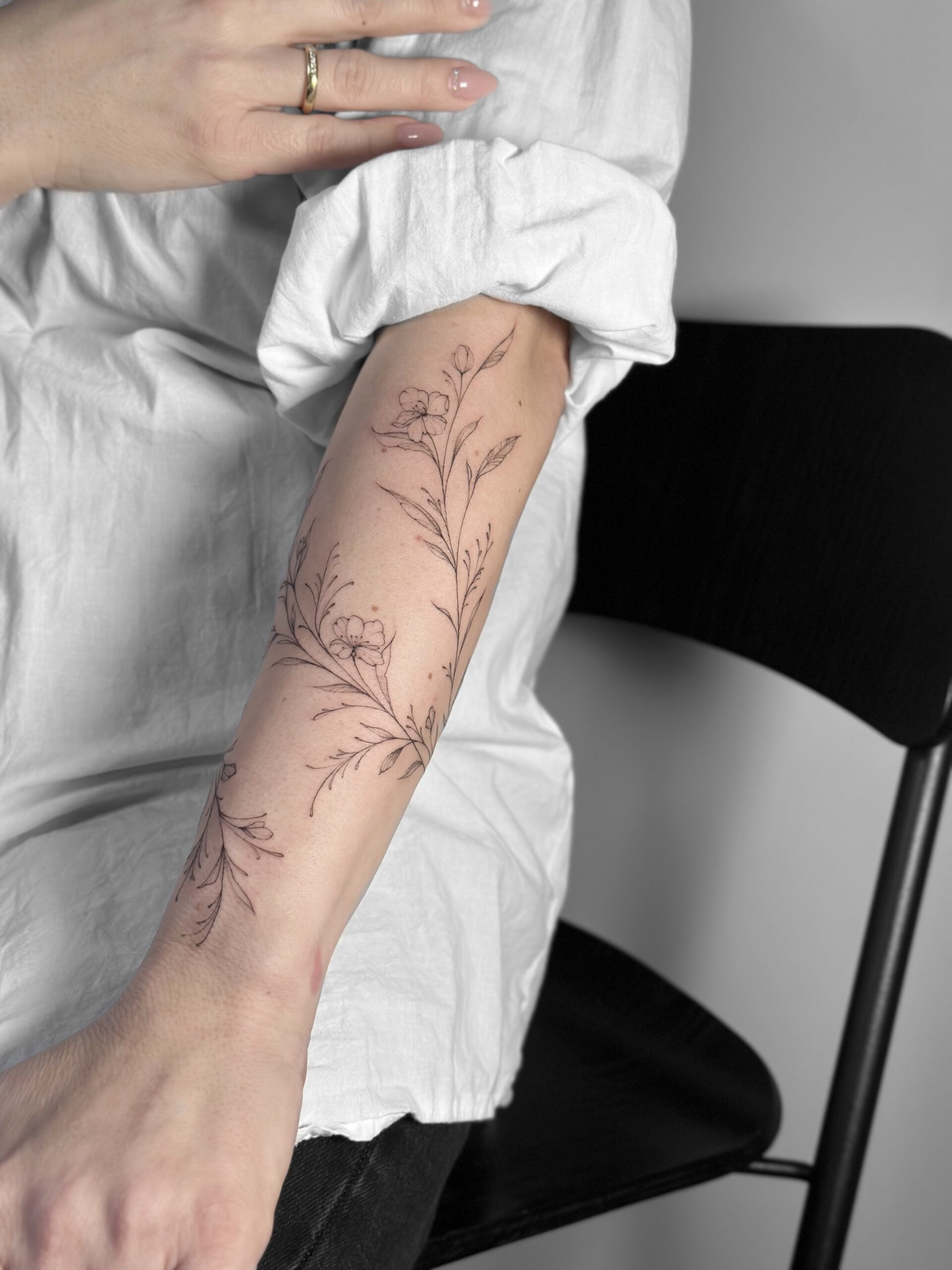 Botanisches fineline Tattoo mit Zweigen und Blüten am Unterarm in Berlin