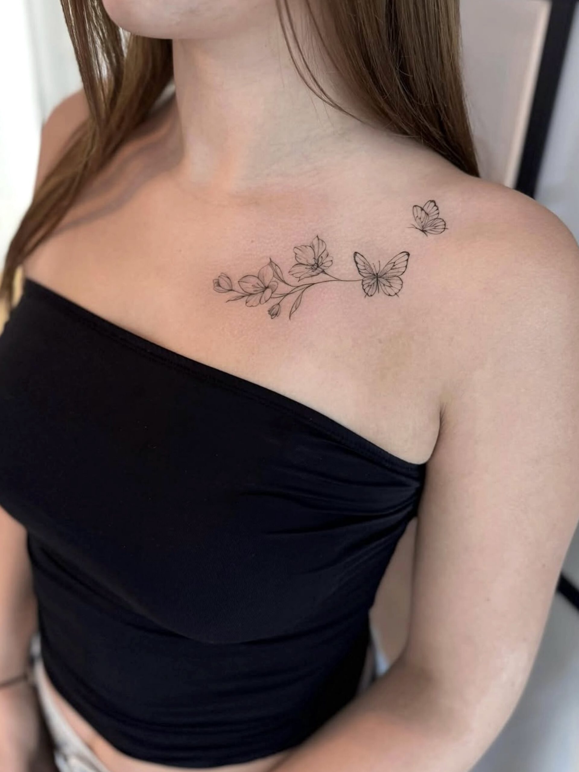 Fine Line Schmetterling-Tattoos mit Zweig am Schlüsselbein in Berlin