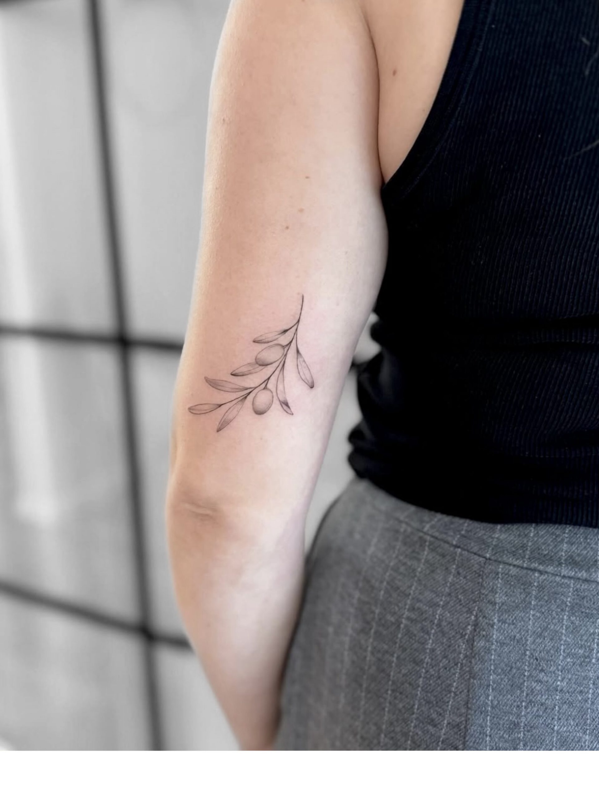 Fine Line Zweig-Tattoo mit Blättern am Oberarm in Berlin-Charlottenburg