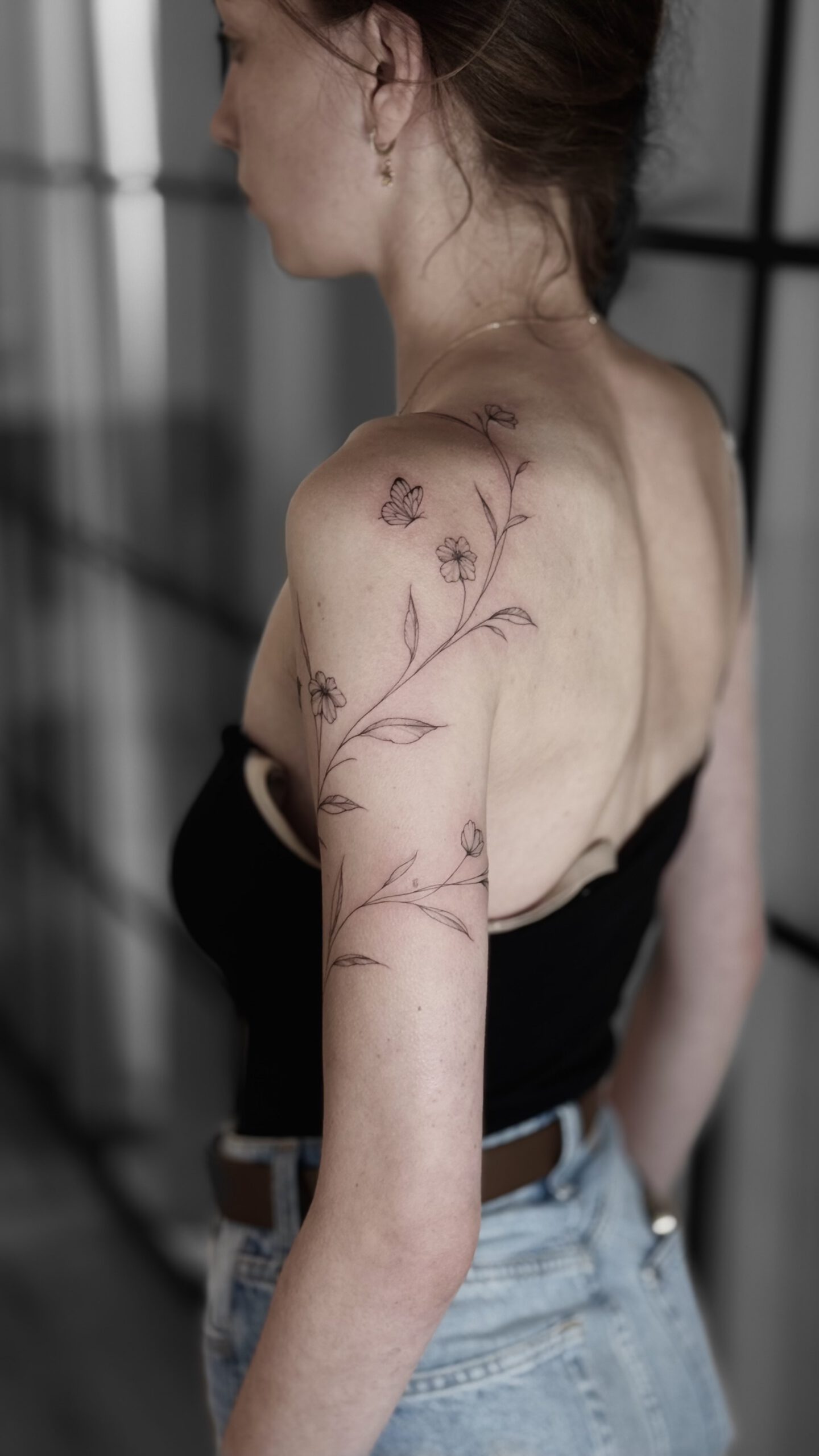 fineline Blumen-Tattoo mit Zweigen an Oberarm und Rücken in Berlin