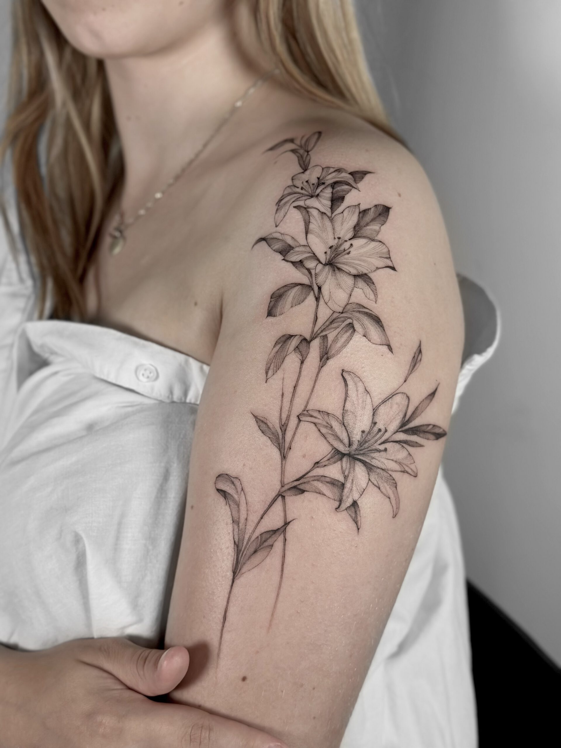 Fineline Lilien-Tattoo an Schulter und Oberarm in Berlin-Schöneberg