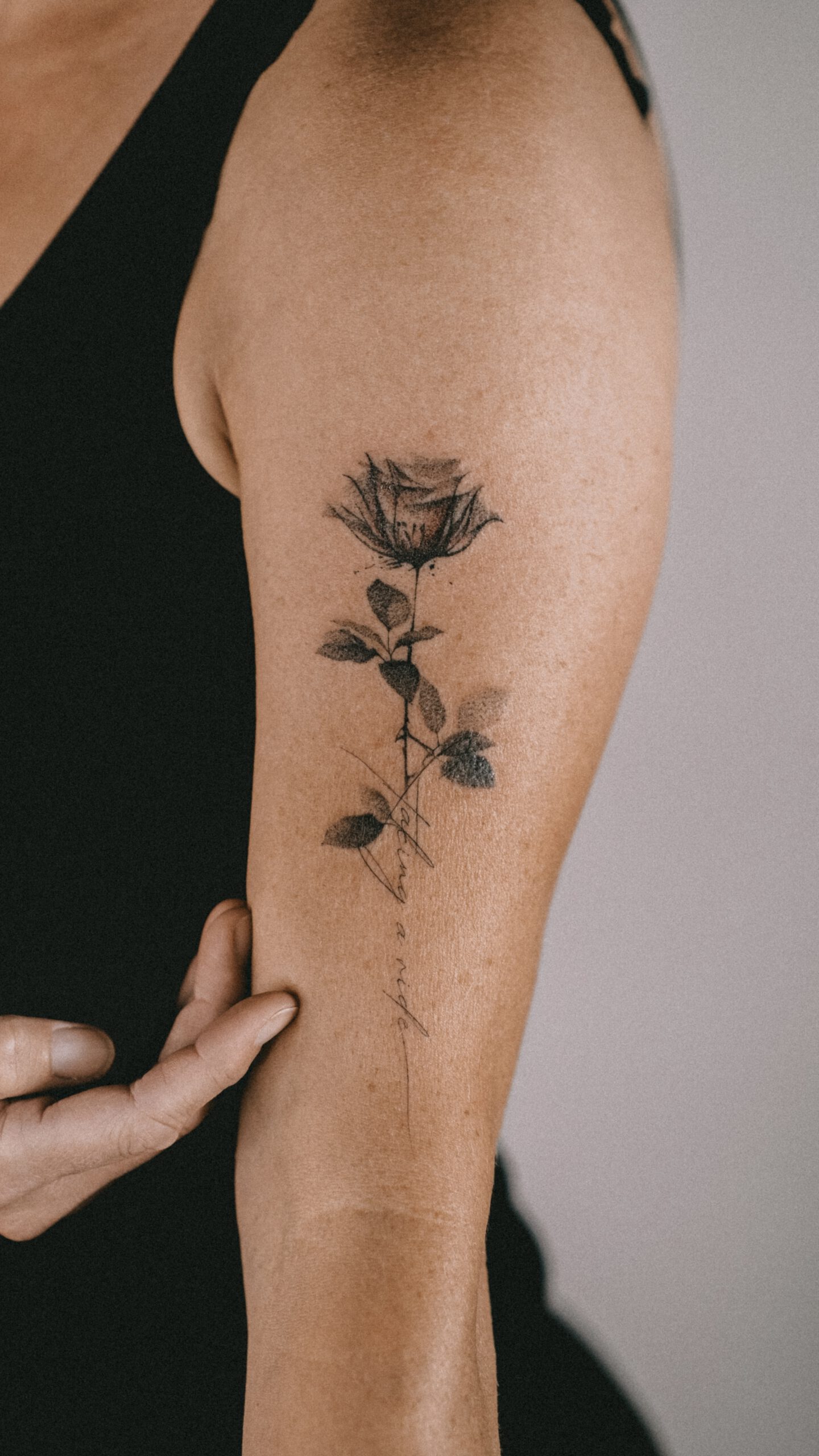 Fineline Rose-Tattoo mit Schriftzug am Oberarm in Berlin-Charlottenburg