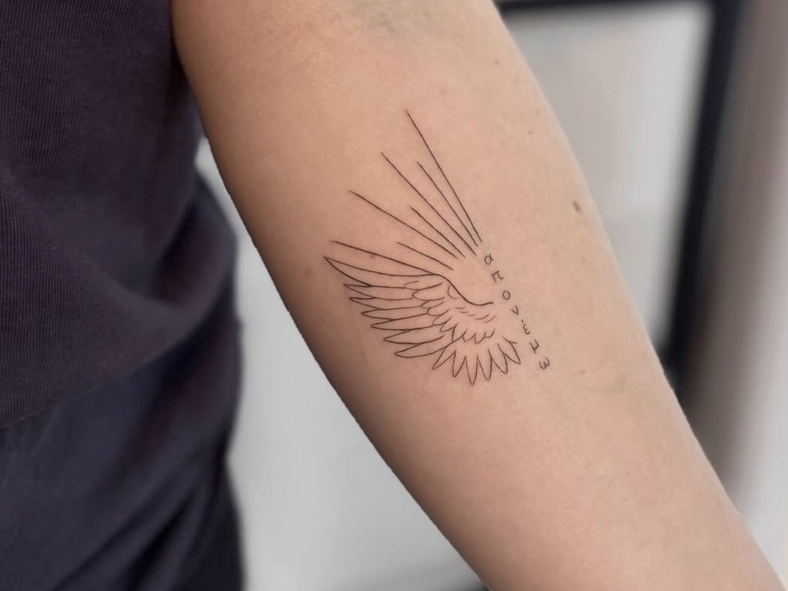 Fineline Flügel-Tattoo mit Federstruktur am Unterarm in Berlin-Schöneberg