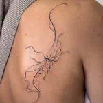 Elegantes, geschwungenes Fine Line Tattoo einer abstrakten Blüte auf dem Schulterblatt.