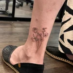 Botanisches Fine Line Tattoo mit feinen Rosen und Wildblumen am Fußknöchel.