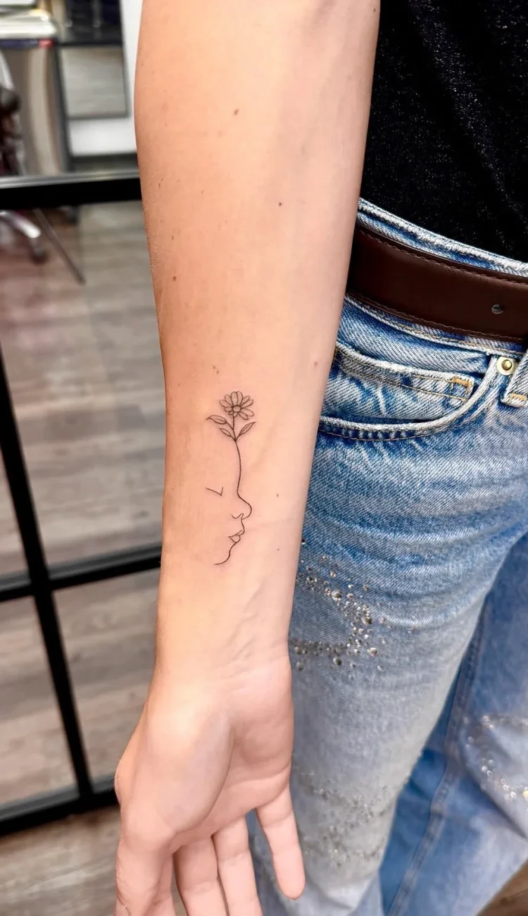 Filigranes Fine Line Tattoo eines Kinderprofils mit blühender Blume am Unterarm, gestochen im BS Tattoo Studio Berlin.