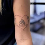 Zartes Fineline Herz Tattoo am Oberarm mit einer liebevollen Mutter-Kind-Darstellung, floralen Details und feiner Linienführung – persönliches Tattoo in Berlin.
