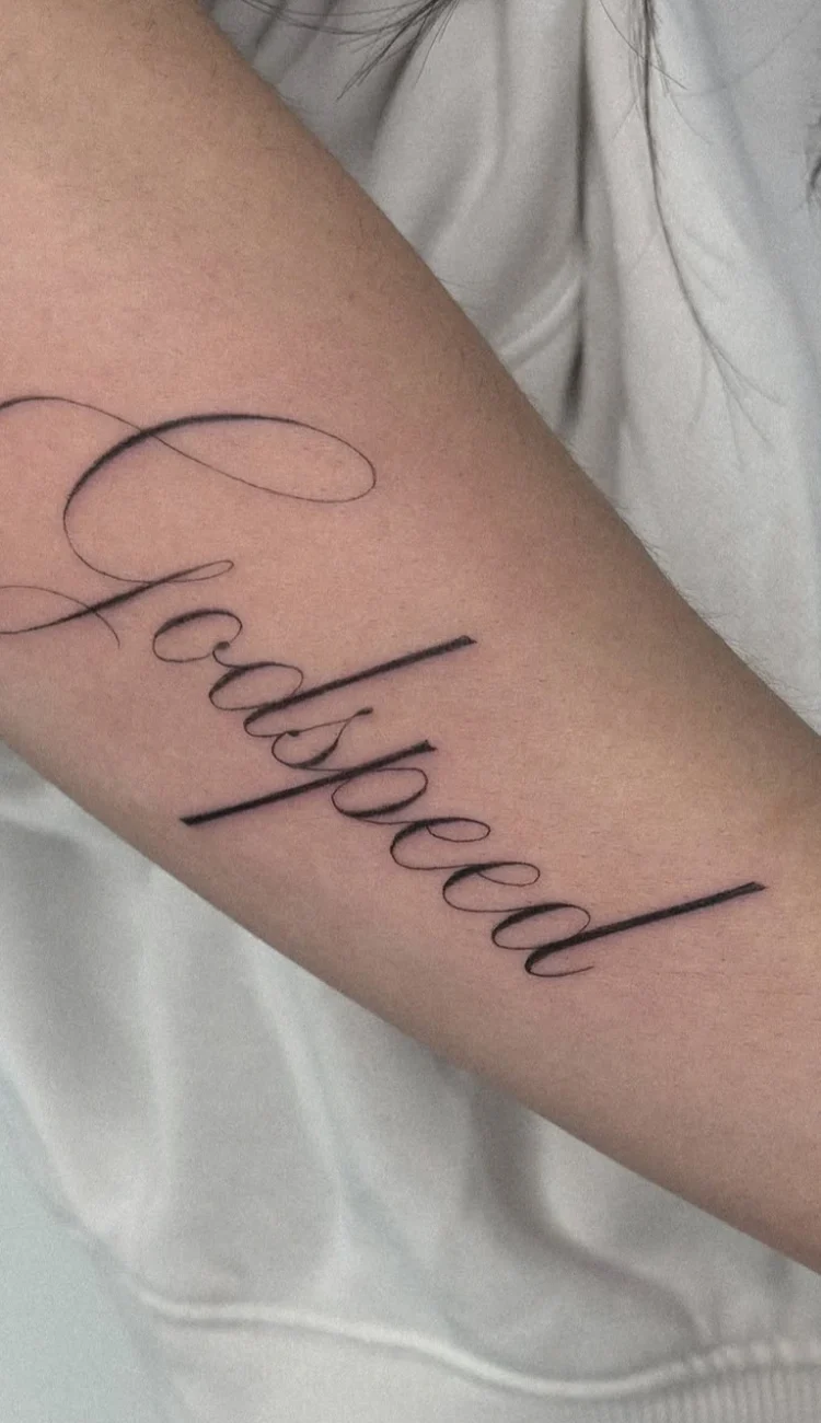 Elegantes Fine Line Schriftzug Tattoo mit dem Wort Godspeed in geschwungener Calligraphy-Schrift am Unterarm.