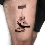 Hochdetailliertes Microrealismus Black and Grey Tattoo eines Paars aufgehängter Air Jordan Sneaker auf dem Oberschenkel, aus einem Berlin Tattoo Studio.
