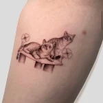 Süßes, feines Microrealismus Tattoo von zwei Katzen auf einem Kratzbaum, umrahmt von Kleeblättern, aus unserem Schöneberg Tattoo Studio.