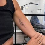 Zartes kleines Fineline Blumentattoo am Oberarm mit filigranen Blüten und feinen Zweigen – minimalistisches Tattoo-Design in Berlin-Schöneberg.