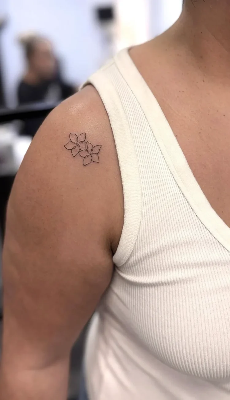 Zartes kleines Fineline Blumentattoo an der Schulter mit mehreren filigranen Blüten – minimalistisches und dezentes Tattoo-Design in Berlin.
