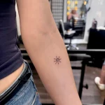 Dezentes Micro Tattoo einer kleinen, spiralförmigen Sonne in feinsten Linien auf dem Unterarm.