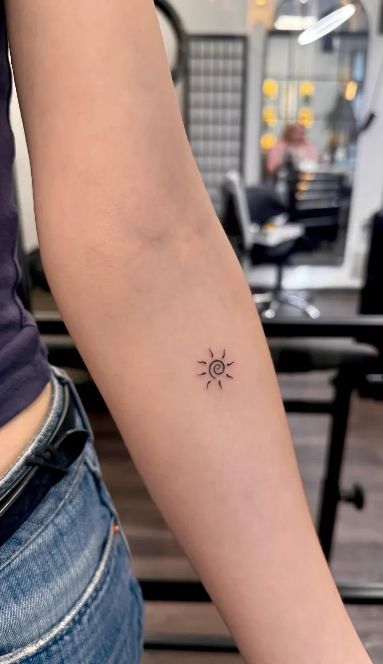 Dezentes Micro Tattoo einer kleinen, spiralförmigen Sonne in feinsten Linien auf dem Unterarm.
