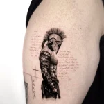 Detailliertes Black & Grey Microrealismus Tattoo eines spartanischen Kriegers mit Helm und Schriftzug auf dem Arm, gestochen von Black Smoke Tattoo Berlin.