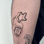 Kreatives Microrealismus Tattoo eines Tamagotchi-Spiels mit Sternenanhänger am Arm.