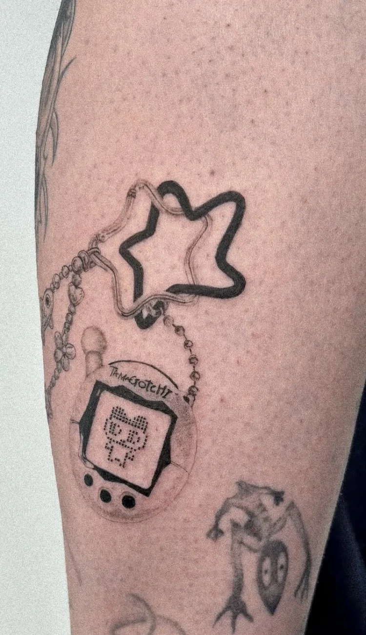 Kreatives Microrealismus Tattoo eines Tamagotchi-Spiels mit Sternenanhänger am Arm.