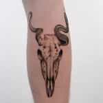 Detailliertes Black & Grey Tattoo eines Tierschädels mit gewundener Schlange an der Wade.