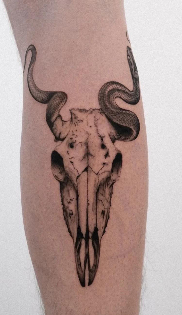 Detailliertes Black & Grey Tattoo eines Tierschädels mit gewundener Schlange an der Wade.