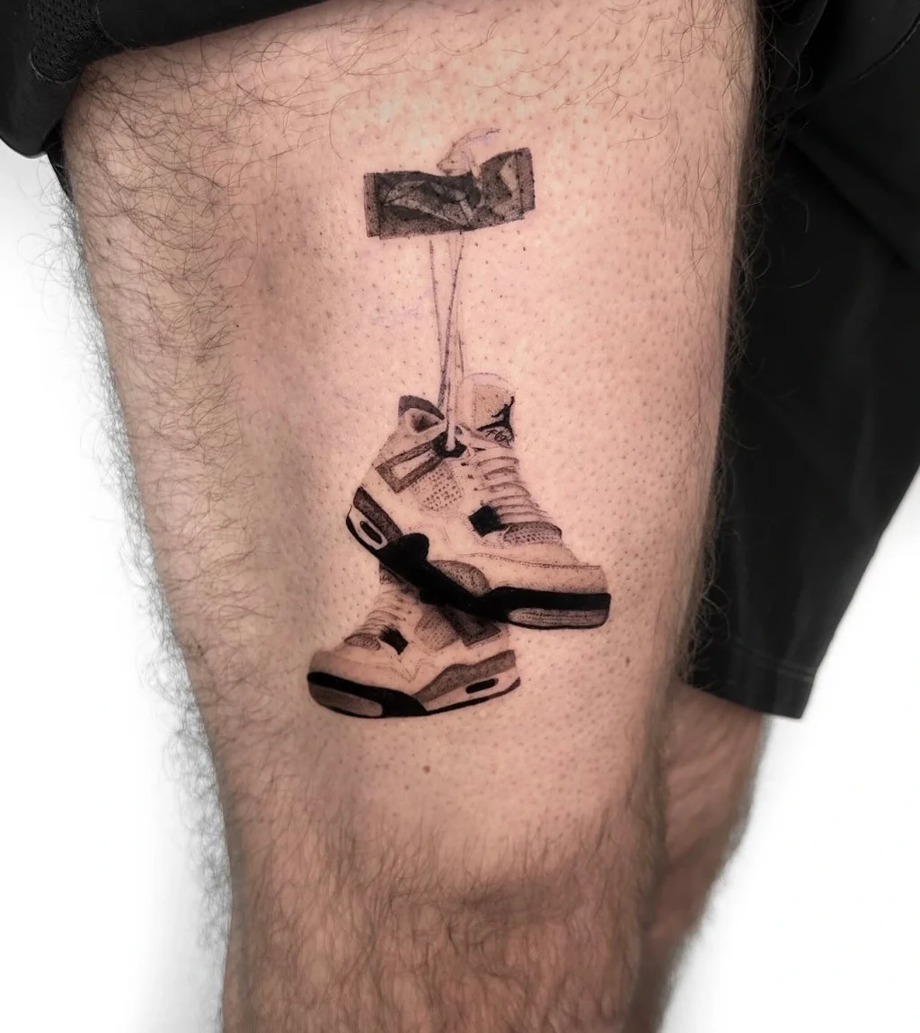 Hochdetailliertes Microrealismus Black and Grey Tattoo eines Paars aufgehängter Air Jordan Sneaker auf dem Oberschenkel, aus einem Berlin Tattoo Studio.